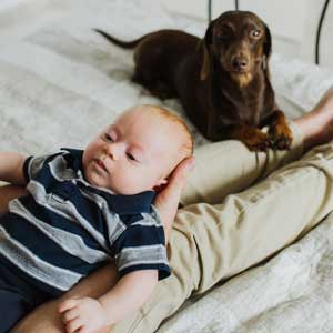 Dog sits at father’s feet while he holds baby